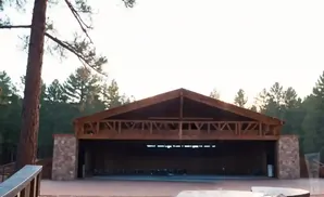 Outdoor wooden amphitheater with stone accents, surrounded by pine trees.