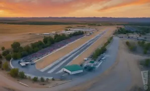 Aerial view of a drag strip with bleachers, a building, and a sunset sky.