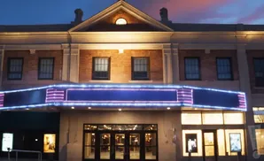 A movie theater facade at dusk with a lit marquee and entrances.