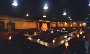 Dimly lit comedy club with rows of tables and a stage area.
