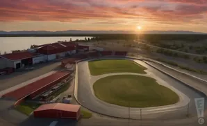 Aerial view of a racetrack with grandstands and buildings at sunset.