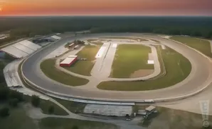 Aerial view of a race track at sunset with a warm orange sky and surrounding trees.