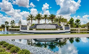 Entrance to a community with palm trees, fountains, and a reflective pond.