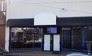 A storefront with a blank arched sign, dark awning, and large windows outlined in blue neon lights.