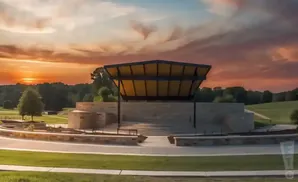 An amphitheater stage with a covered roof and stone seating is set against a sunset sky.