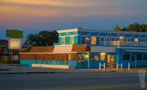 A bright blue motel with a thatched roof overhang at sunset.