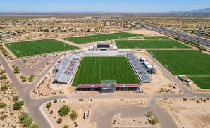 Aerial view of a soccer stadium with multiple practice fields and surrounding desert landscape.