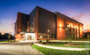 Modern brick building at dusk with bright exterior lights and a colorful sunset sky.