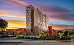 A modern hotel complex with a tall, patterned tower at sunset.