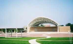 An outdoor amphitheater with a curved, white metal roof, brick walls, and a paved area.