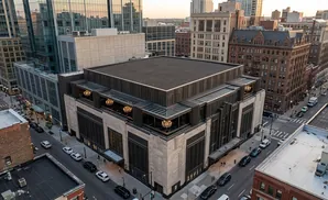Aerial view of a modern building with a flat roof, surrounded by city buildings and streets with cars.