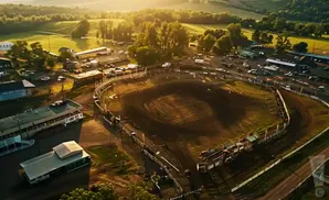 Aerial view of a rodeo arena at sunset, with grandstands and parked cars.