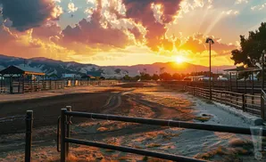 Golden sunset over a dusty ranch with mountains in the background.