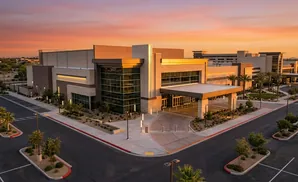 Modern medical center building at sunset with palm trees and desert landscaping.