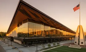 Modern building with glass facade and overhanging roof, flying American flag at sunset.