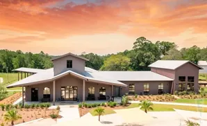 A modern brown building with a silver roof sits under a vibrant orange sky, surrounded by trees.