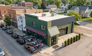 Aerial view of a green building with outdoor seating and parked cars on a sunny day.