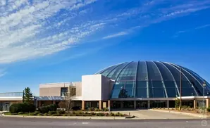 Modern building with a large glass dome roof under a blue sky with scattered clouds.