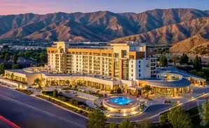 An aerial view of a modern hotel with a pool and mountains in the background at sunset.