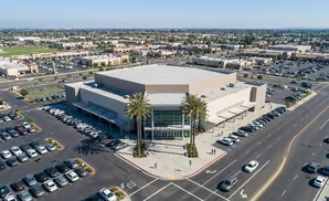 Aerial view of a large convention center or arena with surrounding parking lots and retail buildings.