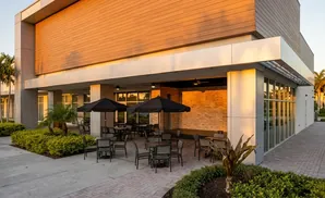 An outdoor seating area with tables, chairs, and black umbrellas in front of a building with a wooden exterior.