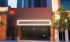 Modern building entrance with glowing rectangular sign and glass doors.