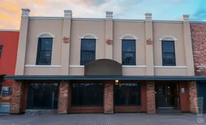 A tan two-story building with arched windows on the second floor and large dark windows on the first.