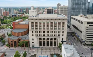 Aerial view of a grand stone building with columns, surrounded by other city buildings and green spaces.