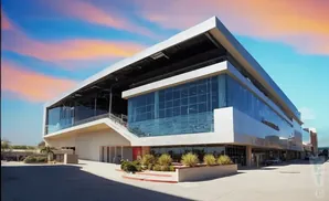 Modern, multi-story building with large glass windows and a metal roof under a colorful sky.