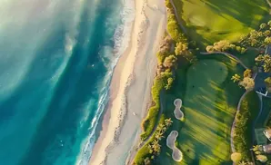 Aerial view of a beach and golf course with turquoise water and lush green fairways.