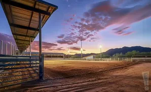 Equestrian arena at sunset with dramatic clouds, lights, and mountains in the background.