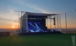 An outdoor stage is set up at sunset, with blue spotlights shining on the empty stage.