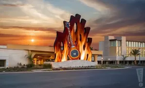 Flaming guitar sculpture in front of a modern building at sunset.