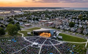 Aerial view of an outdoor concert with a large audience and orchestra on stage.