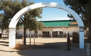 White archway leading to a building with a green roof and a sign that says 