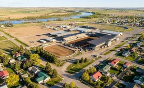 Aerial view of a rodeo arena and grandstands next to a curving racetrack, with a river and rolling hills in the background.