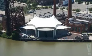 An outdoor concert venue with a white tent structure on a pier beside a body of water.