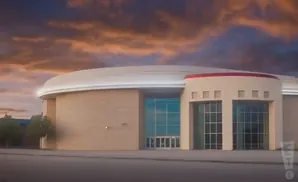 A large, rounded building with tan brick and a white roof, under a dramatic, cloudy sky.