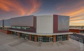 Aerial view of a modern commercial building with a curved glass storefront and metal siding, under a colorful sunset sky.