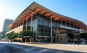 Modern convention center with glass facade and wavy roof, lit by interior lights.