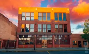 Sunset over a brick building with large windows, reflecting the vibrant orange and pink clouds.