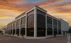 A modern building with large windows and arched entries sits under a dramatic orange sunset.