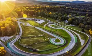 Aerial view of a winding race track surrounded by trees and hills during golden hour.