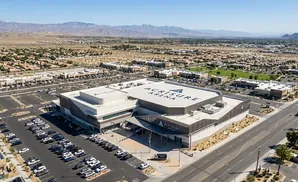 Aerial view of Acrisure Arena in Palm Springs, CA, surrounded by parking lots and commercial buildings, with mountains in the background.