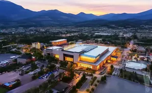 Aerial view of a large, brightly lit building at dusk with mountains in the background.