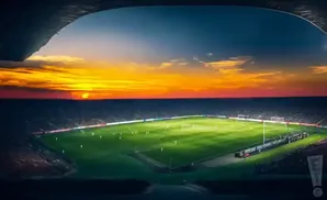 A soccer stadium at sunset, with a bright orange sky over the field and stands.