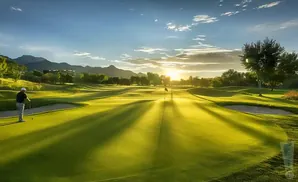 Golfer on a sunlit golf course with mountains in the background.