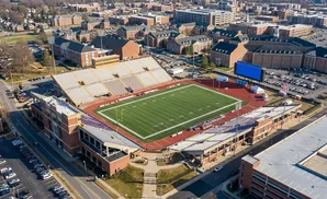 Aerial view of a football stadium with a green field, bleachers, and surrounding campus buildings.