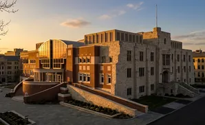 A modern brick and stone building with a curved glass entrance, bathed in warm sunset light.