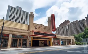 Exterior view of a historic theatre with a large marquee and a tall skyscraper behind it.